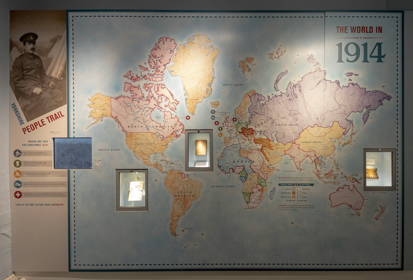 1914 colorful world map exhibit with artifacts and text.