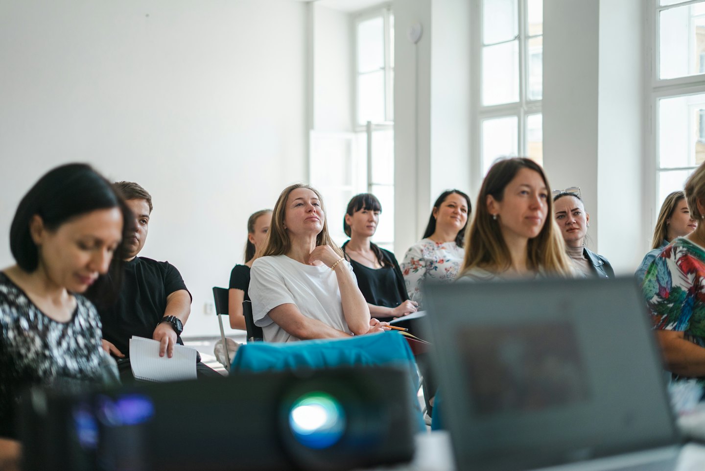 Audience members listening attentively in a bright conference room.