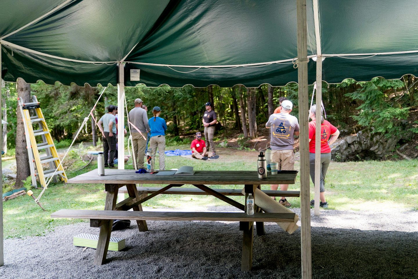 A group gathers for a discussion under a green canopy tent.
