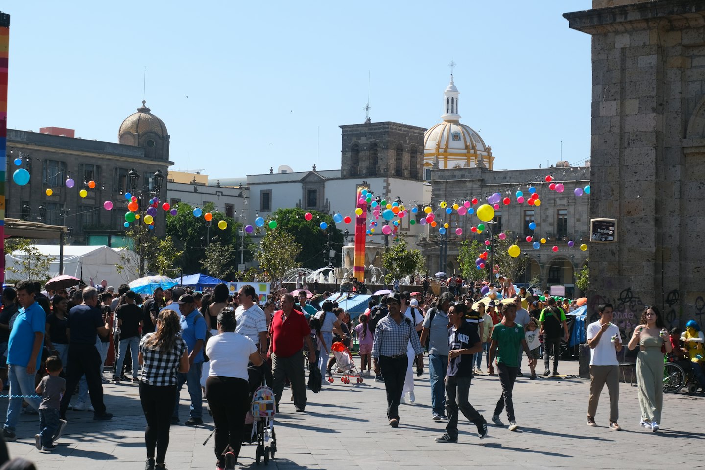 A large crowd walks through a historic square with balloons.